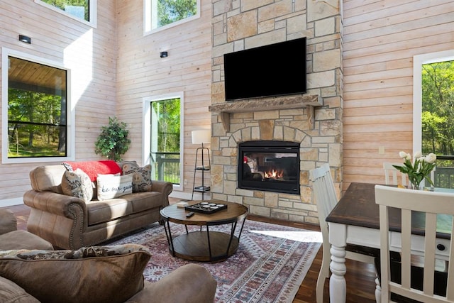 living room with a stone fireplace, wooden walls, a high ceiling, and hardwood / wood-style flooring