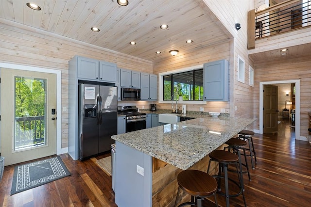 kitchen with appliances with stainless steel finishes, a kitchen breakfast bar, wooden walls, dark wood-type flooring, and wooden ceiling