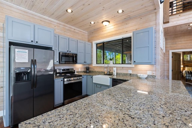 kitchen with appliances with stainless steel finishes, light stone counters, sink, wooden ceiling, and wood walls