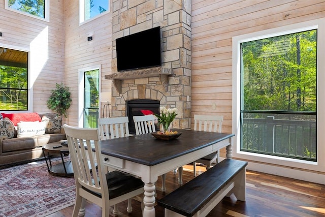 dining area featuring wood walls, a stone fireplace, a towering ceiling, and wood-type flooring