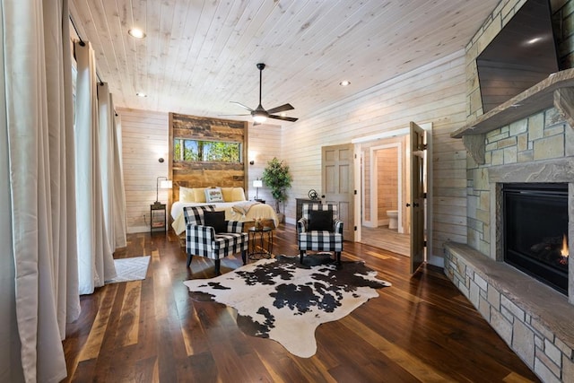 bedroom featuring ceiling fan, wooden walls, wooden ceiling, a fireplace, and dark hardwood / wood-style floors