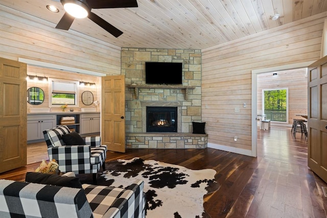 living room with wooden walls, ceiling fan, a fireplace, dark hardwood / wood-style flooring, and wood ceiling