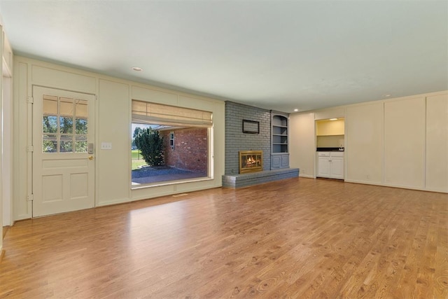 unfurnished living room featuring built in features, a fireplace, and light hardwood / wood-style flooring