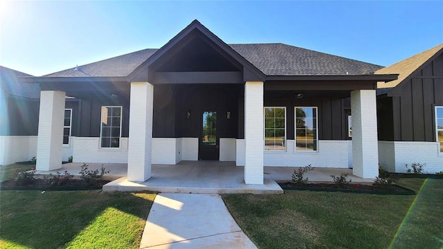 1308 W Harvard Way, Mustang, OK 73064 - doorway to property featuring board and batten siding, roof with shingles, brick siding, a yard, and covered porch