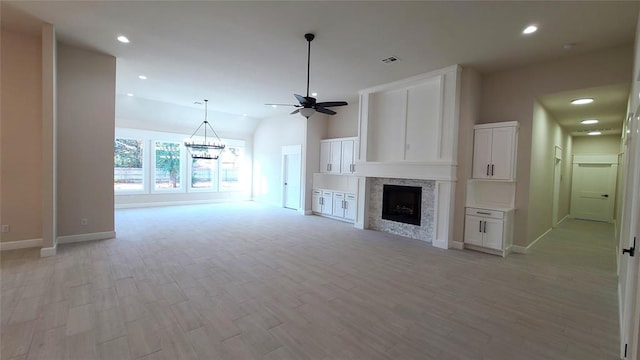 unfurnished living room featuring a large fireplace, light hardwood / wood-style flooring, vaulted ceiling, and ceiling fan with notable chandelier