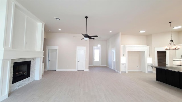 unfurnished living room with ceiling fan with notable chandelier, light wood-type flooring, and a fireplace