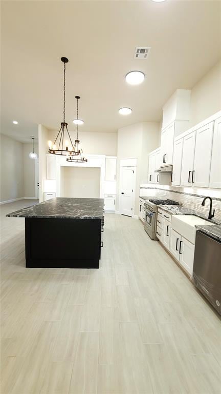 kitchen featuring high end stove, dark stone countertops, white cabinets, a center island, and hanging light fixtures