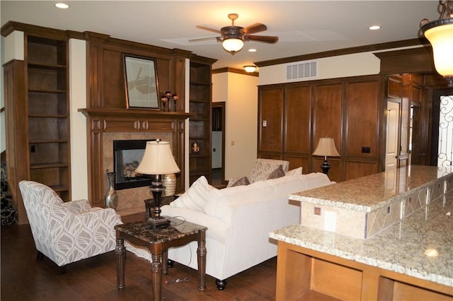 living room with dark hardwood / wood-style floors, ceiling fan, a premium fireplace, and ornamental molding