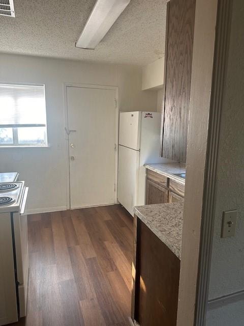 kitchen with a textured ceiling, white refrigerator, range, and dark wood-type flooring