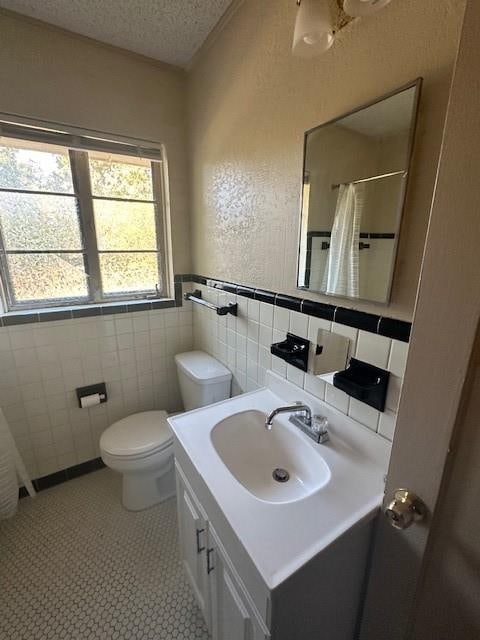 bathroom with vanity, tile patterned flooring, toilet, a textured ceiling, and tile walls