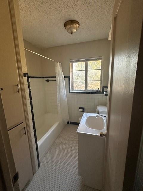 bathroom with a textured ceiling, shower / bath combo with shower curtain, vanity, and tile walls