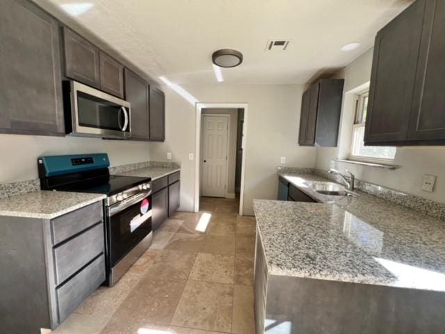 kitchen featuring light stone counters, sink, dark brown cabinets, and appliances with stainless steel finishes