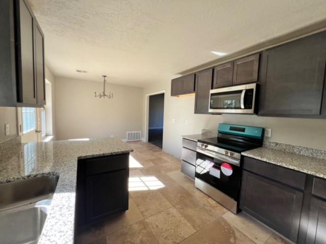 kitchen featuring light stone countertops, an inviting chandelier, decorative light fixtures, dark brown cabinets, and appliances with stainless steel finishes