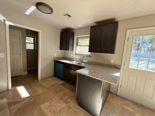 kitchen with dark brown cabinetry, light stone counters, and sink