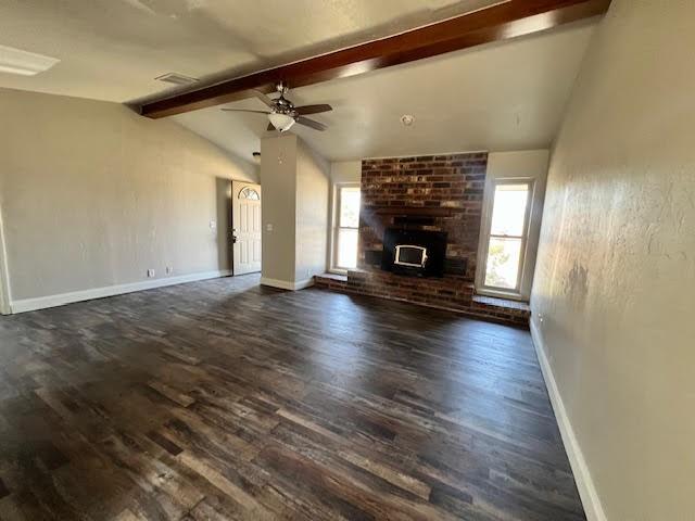 unfurnished living room featuring lofted ceiling with beams, ceiling fan, dark hardwood / wood-style flooring, and a wood stove