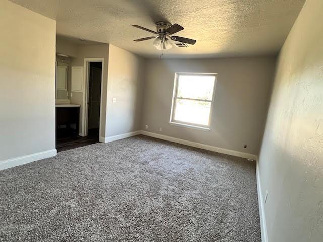 empty room featuring dark colored carpet, ceiling fan, and a textured ceiling