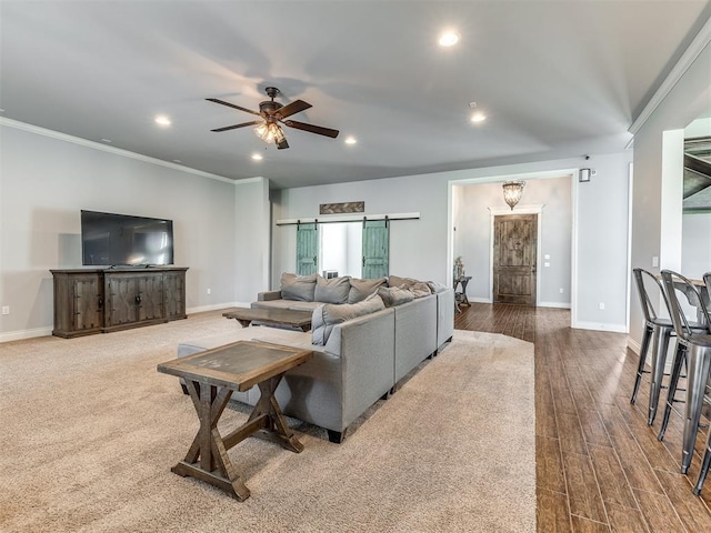 living room featuring hardwood / wood-style floors, a barn door, ceiling fan, and crown molding