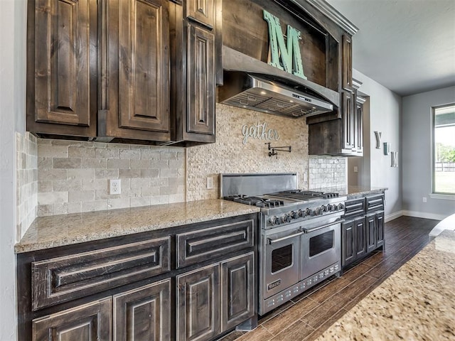 kitchen featuring dark hardwood / wood-style flooring, backsplash, light stone counters, wall chimney range hood, and double oven range