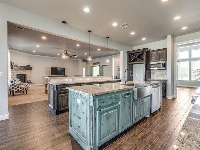 kitchen with a large island with sink, stainless steel appliances, light stone counters, and ceiling fan