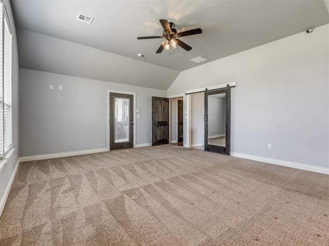 unfurnished bedroom with ceiling fan, a barn door, lofted ceiling, and multiple windows