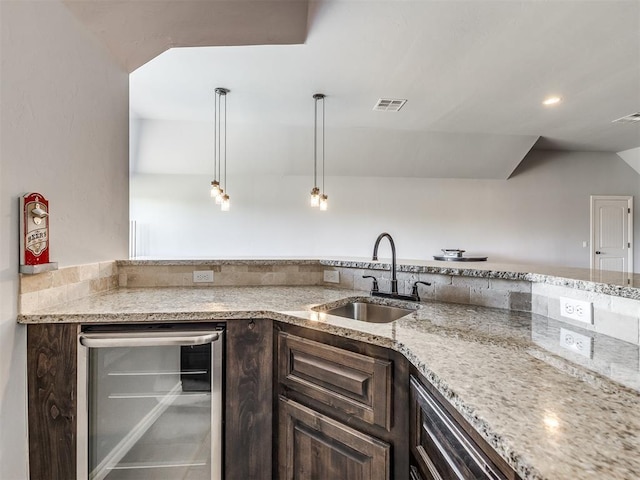 kitchen featuring light stone countertops, dark brown cabinetry, beverage cooler, sink, and hanging light fixtures