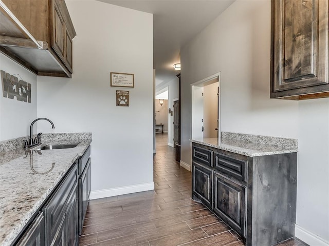 kitchen with light stone countertops, dark brown cabinetry, dark hardwood / wood-style floors, and sink