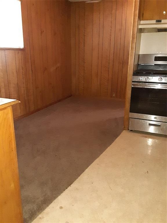 interior space with under cabinet range hood, wood walls, light countertops, stainless steel gas range, and brown cabinetry