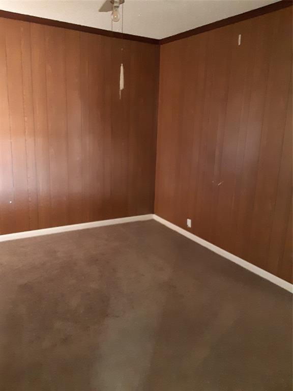 carpeted spare room with ceiling fan, wood walls, and baseboards