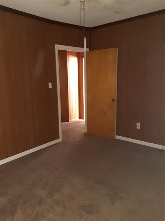 carpeted empty room with wood walls and crown molding