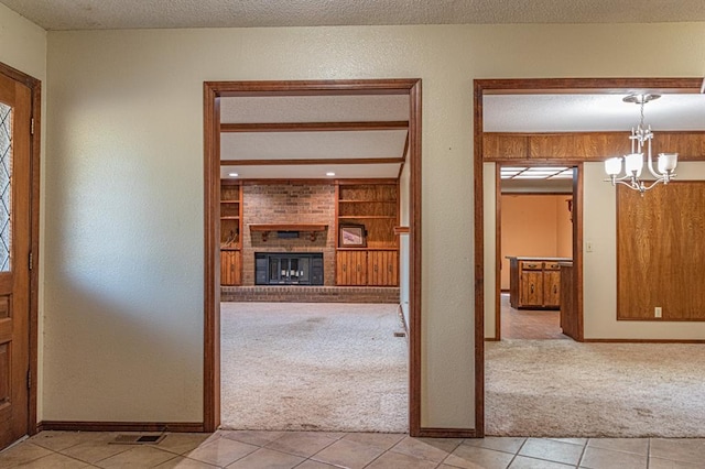 foyer entrance with a chandelier, a fireplace, light colored carpet, and a textured ceiling