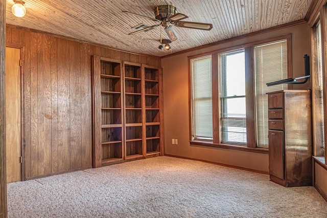 empty room with ceiling fan, wood walls, light colored carpet, and wooden ceiling