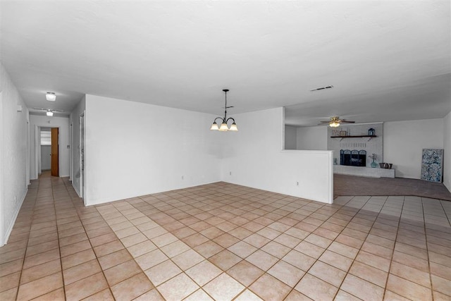 empty room with a fireplace, light tile patterned floors, and ceiling fan with notable chandelier