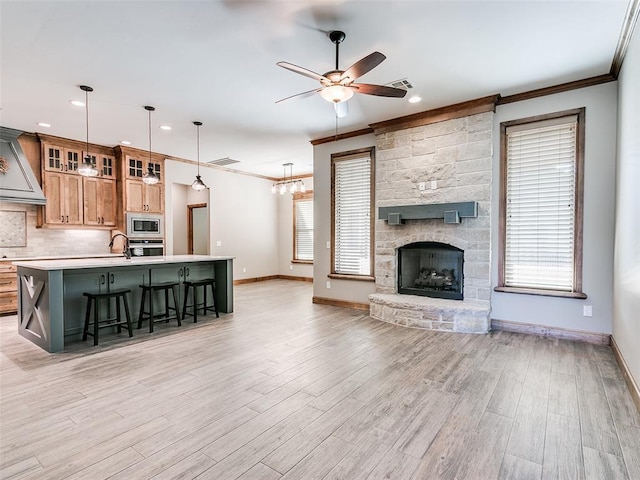 unfurnished living room with crown molding, a fireplace, ceiling fan with notable chandelier, and light wood-type flooring