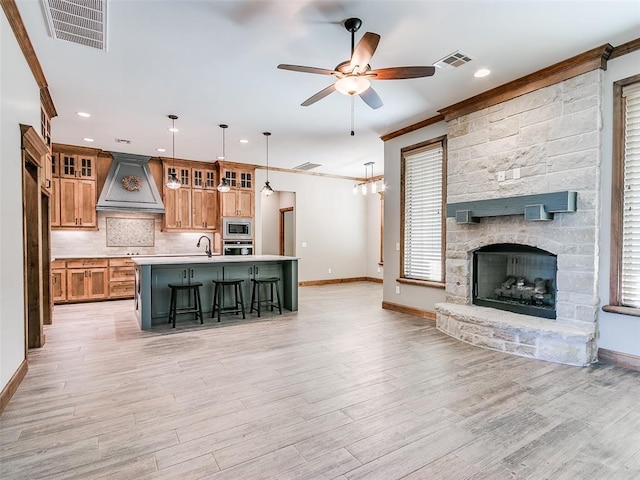 kitchen with stainless steel appliances, pendant lighting, a center island with sink, custom exhaust hood, and light wood-type flooring