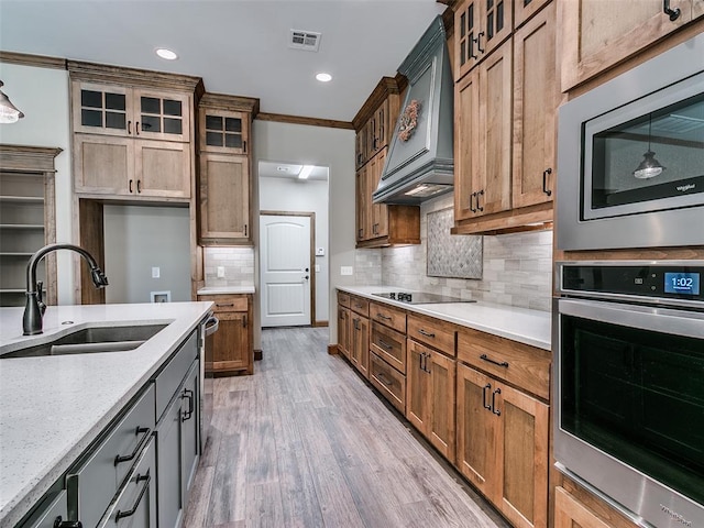 kitchen featuring sink, stainless steel appliances, premium range hood, crown molding, and light hardwood / wood-style floors