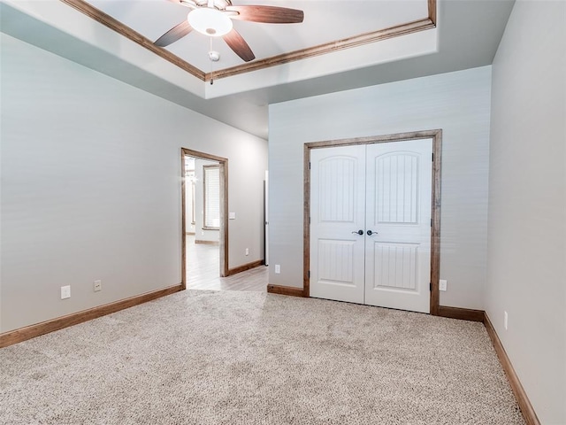 unfurnished bedroom featuring ceiling fan, a raised ceiling, light carpet, and a closet