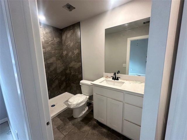 bathroom featuring vanity, a tile shower, and toilet