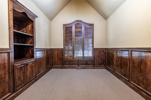 unfurnished room with carpet floors, wooden walls, and vaulted ceiling