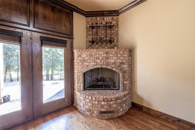 unfurnished living room with french doors, hardwood / wood-style flooring, a brick fireplace, and crown molding