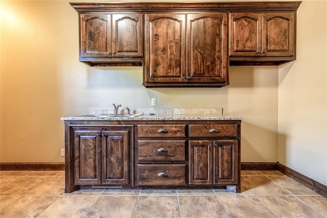 bar with dark brown cabinetry, light stone counters, and sink