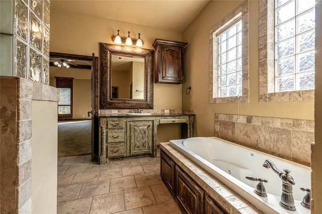 bathroom with ceiling fan, a relaxing tiled tub, and vanity