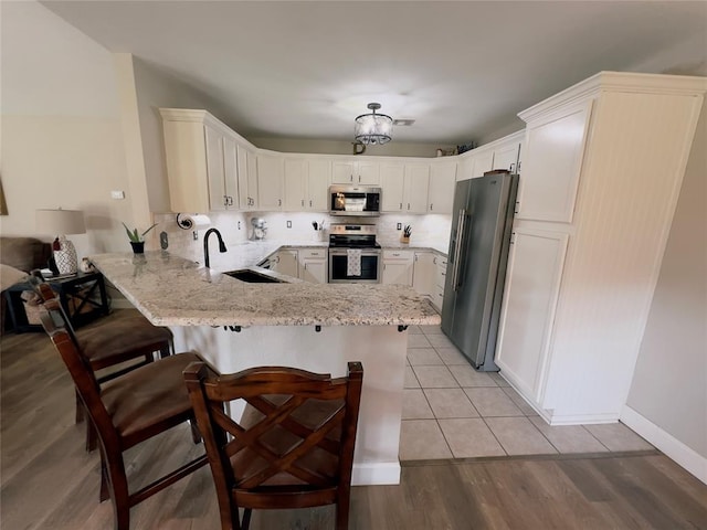 kitchen with sink, stainless steel appliances, kitchen peninsula, a breakfast bar, and light wood-type flooring