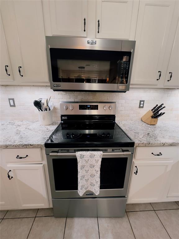 kitchen with tasteful backsplash, light stone counters, light tile patterned floors, and appliances with stainless steel finishes