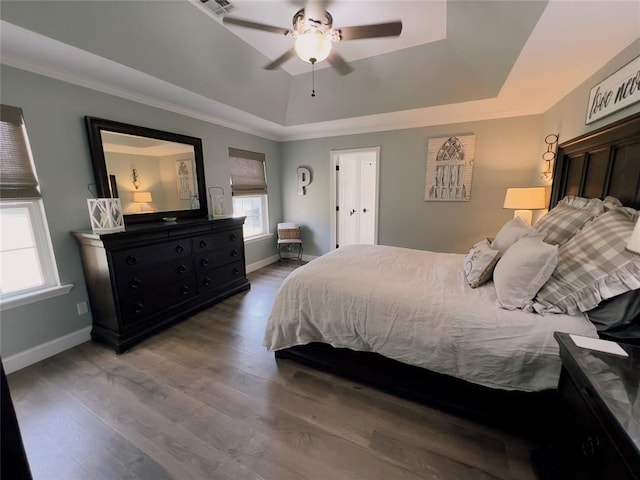 bedroom featuring a tray ceiling, multiple windows, ceiling fan, and hardwood / wood-style floors