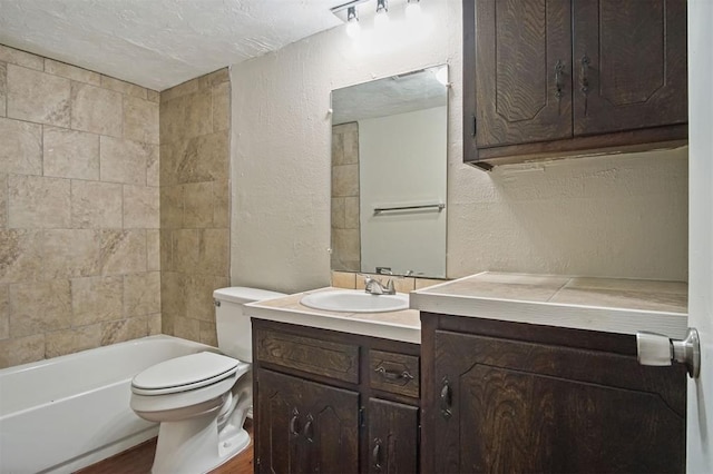 full bathroom with vanity, a textured ceiling, toilet, and tiled shower / bath