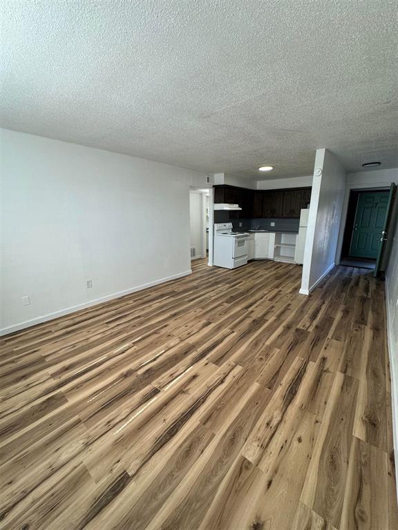 5825 NW 34th St, Oklahoma City, OK 73122 - unfurnished living room featuring wood finished floors, a textured ceiling, and baseboards