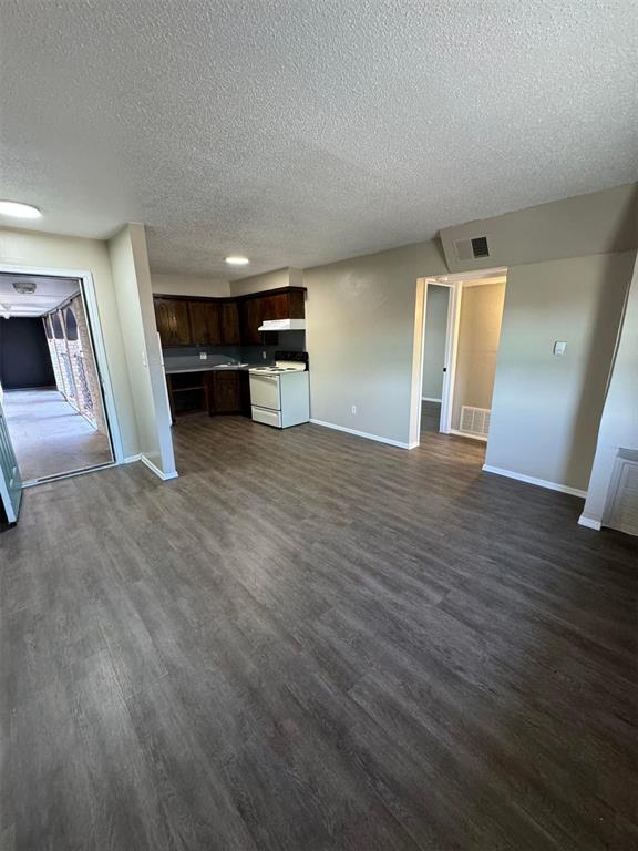5825 NW 34th St, Oklahoma City, OK 73122 - unfurnished living room with a textured ceiling, dark wood-style flooring, and baseboards