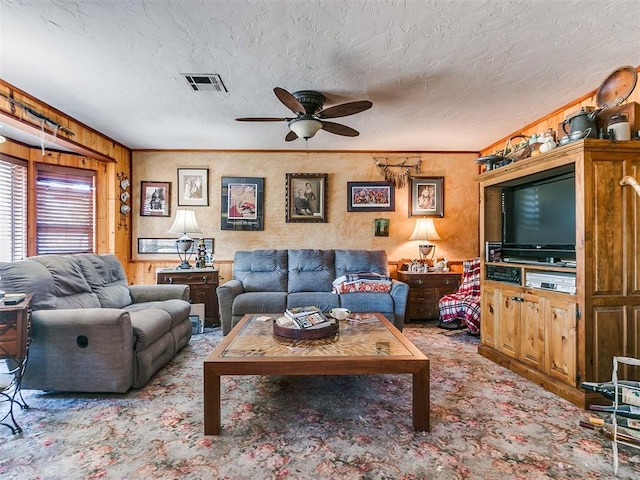 living room featuring carpet, ceiling fan, wood walls, and a textured ceiling