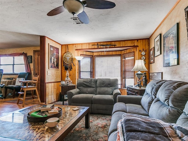 living room with hardwood / wood-style flooring, ceiling fan, crown molding, and wooden walls