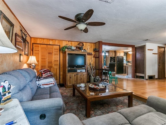 living room with a textured ceiling, hardwood / wood-style flooring, ceiling fan, and wood walls